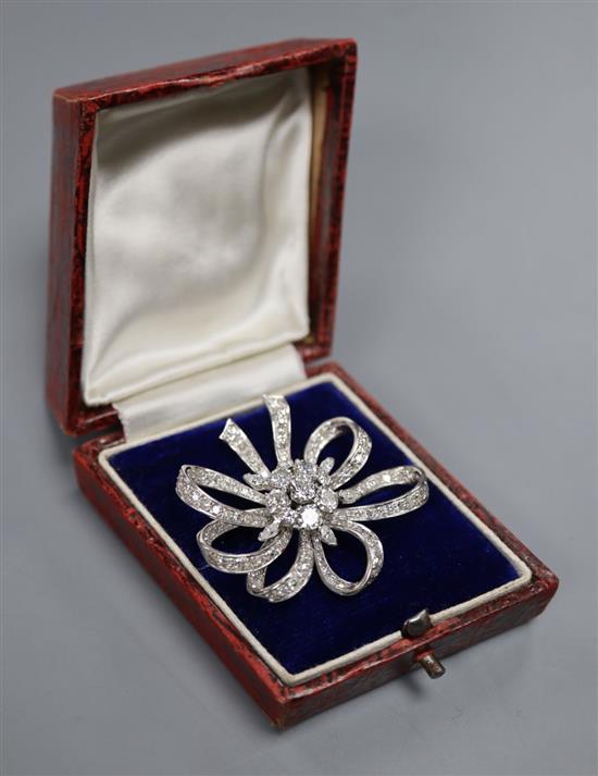 A mid 20th century white metal and diamond cluster set ribbon scroll brooch, 36mm, gross 15.6 grams.